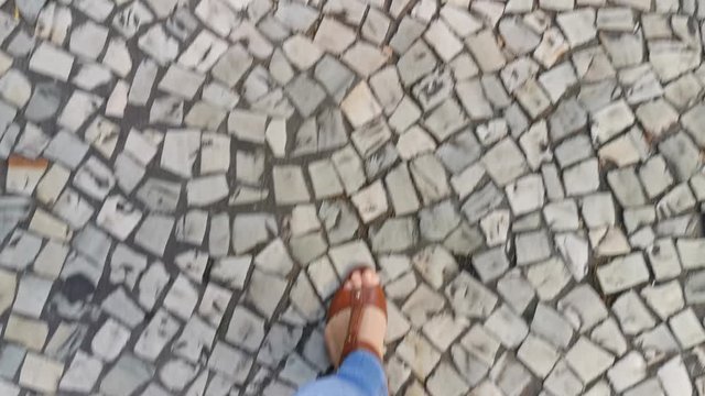 POV. Feet in brown sandals, classic blue jeans, walk on the sidewalk.