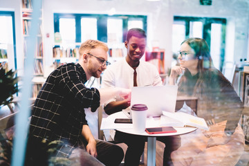 Delight multicultural hipster guys browsing dunny web articles during laptop networking in university campus, cheerful male and female millennials searching positive medial files on netbook