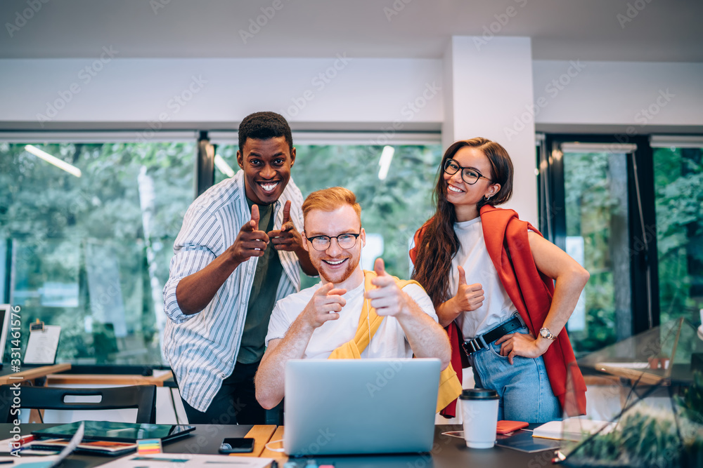 Sticker Cheerful multiracial colleagues smiling and pointing at camera