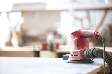 Red orbital sander close-up on the background of a carpentry workshop. DIY wooden furniture concept