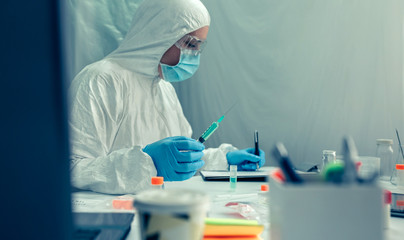 Unrecognizable female scientist with bacteriological protection suit investigating a vaccine in the...