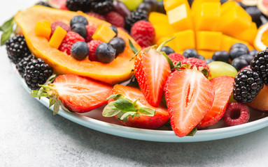 Colorful fruit platter pomegranate papaya oranges grapes berries on plate on white, selective focus