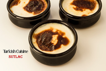 Traditional Turkish Style Baked Rice Pudding in casserole,clay dessert bowl on white surface with Turkish Cuisine,Sutlac writing near bowl.