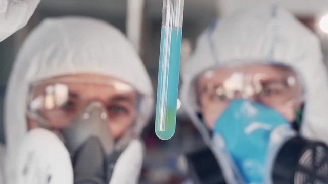 closeup of scientists in protective suits are conducting laboratory testing of blue matter in vitro