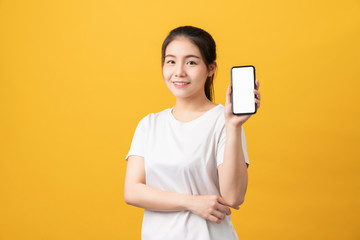 Naklejka premium Cheerful beautiful Asian woman holding smartphone and typing message on light yellow background.