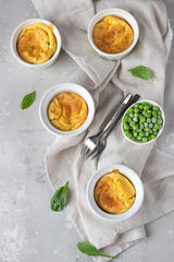 Cheese souffle with green peas in a white ceramic ramekin on a grey linen napkin. Light grey concrete background. 