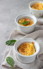 Cheese souffle with green peas in a white ceramic ramekin on a grey linen napkin. Light grey concrete background. 