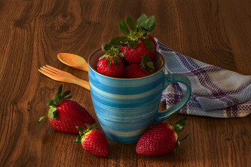 Blue mug with strawberries, wooden fork and teaspoon, and napkin