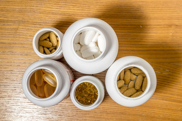 Various tablets and capsules in jars lie on a wooden surface