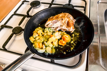 Meat and vegetables are cooked in a pan on the gas stove