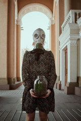 girl in a gas mask and a dress with a plant in her hands during quarantine, in an empty city