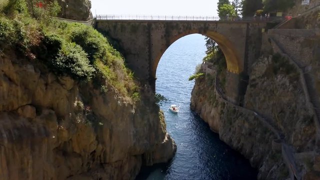 Fiordo di Furore village arch bridge leading to Mediterranean sea, a boat is standing by, Amalfi coast Italy, Aerial dolly in reveal shot