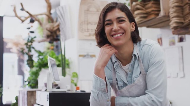 Female owner of florists shop standing behind store sales desk looking into camera and smiling - shot in slow motion