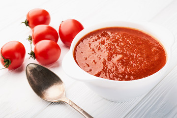 Tomato soup in a white bowl and fresh tomatoes on the table