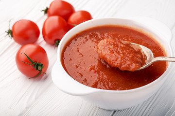 Tomato soup with a spoon scooping soup and fresh tomatoes on the table