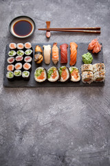 Composition of different kinds of sushi rolls placed on black stone board