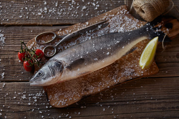 Sea bass fish on the dark wooden background with salt, tomatoes cherry and lemon