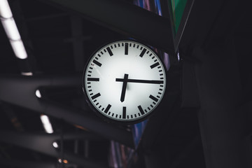 A big white clock is hanging on the wall at train station in the evening.