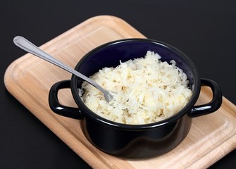 Sauerkraut in the pot. Sauerkraut (fermented or pickled cabbage) on a chopping board, black background
