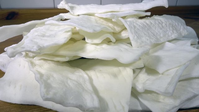 Close circular dolly shot of white rawhide dog dental chews in a pile on a pine counter / worktop.