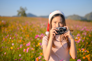 Portrait of young attractive Asian woman wearing Santa hat, travel and visiting cosmos flowers field in Chiang Rai Province of Thailand. Conceptual shot of people tourism and vacation.