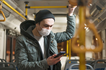 Side view of man with medical mask looking at his phone on the bus