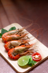 Cooked shrimp placed on a wooden plate, decorated with lime, tomatoes and fresh vegetables, cement background, Copy space for text