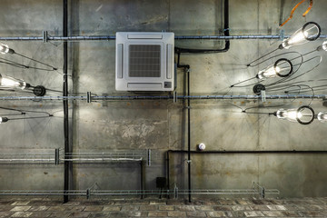 looking up on gray concrete ceiling with halogen spots and edison lamps in loft office room with air conditioning and orange ventilation pipe