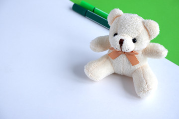 Beautiful beige  bear, colored markers green and light green on a green and white background. Soft toy. School supplies.  Suitable for advertising backgrounds and greeting cards