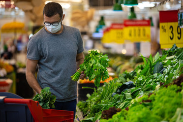 Alarmed male wears medical mask against coronavirus while grocery shopping in supermarket or store-...