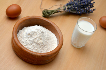flour in a wooden bowl  and a glass of milk on the table