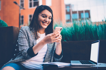 Overjoyed young freelance woman using smartphone in street