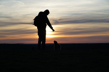 Silhouette of a man and his jumping poodle dog against orange sunset 