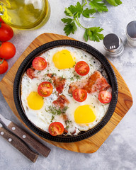 Tasty breakfast with fried eggs, bacon and vegetables on a frying pan. Morning breakfast concept. Closeup. Top view