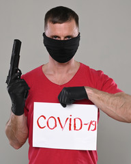 Man in black mask with a gun and  banner with the inscription Covid-19