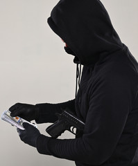 Man in black mask and hoody with a gun and pack of dollars