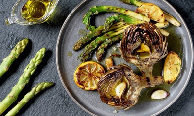 artichoke and asparagus grill. Tasty vegetables are first cooked for a couple, then fried on a grill, poured with olive oil and spices. spring vegetables.background black slate and plate as 