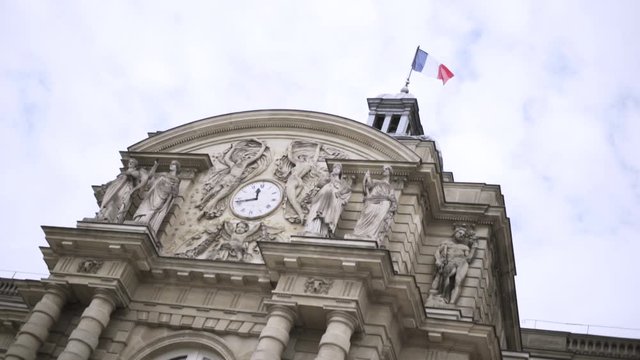French flag waving in the wind on a historic building, architecture concept. Action. Bottom view of a beautiful old building with sculptures and clock.