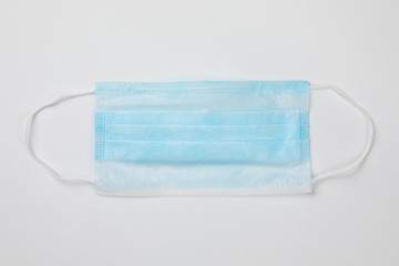 Coronavirus prevention typical 3-ply blue surgical medical mask with rubber ear straps on white background. Hygiene corona virus protection concept. Flat lay.