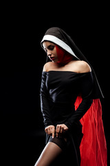 attractive sexy nun posing in black dress, stockings and red scarf, isolated on black