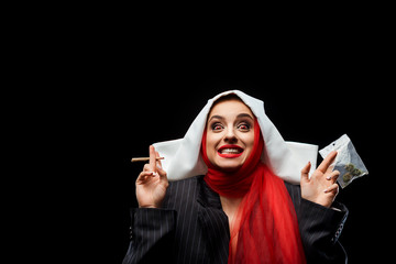excited demoniac nun holding marijuana joint and buds isolated on black