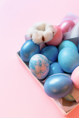 Still life with easter decorated eggs in a box on a pink background.