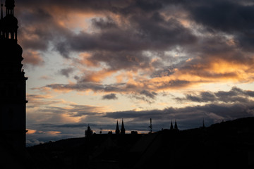 A sillhoute off a city in front of a cloudy sun illuminated yellow and grey sky 