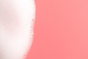 Foam texture border from soap, shampoo or cleanser on pink background. Close-up, macro