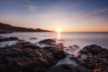 Fototapeta premium Waves washing onto rocky Corsica coastline at sunset