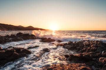 Waves crashing onto rocky Corsica coastline at sunset