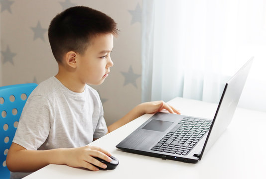 A Small Boy Samir Is Sitting At A Table Playing On The Computer And Phone