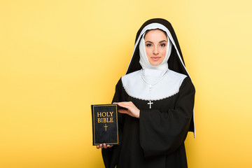 beautiful smiling nun holding holy bible on grey