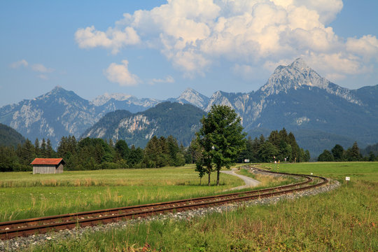 old curved railroad tracks with level crossing and haystack in an idyllic landscape in the European Alps