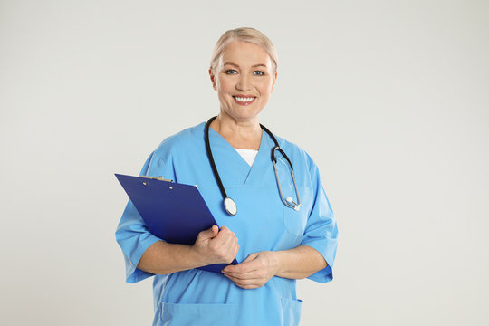 Mature doctor with clipboard on light grey background
